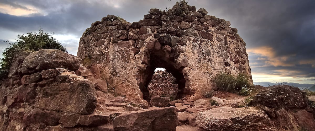 A large rock formation with a central archway, surrounded by smaller rocks and sparse vegetation.