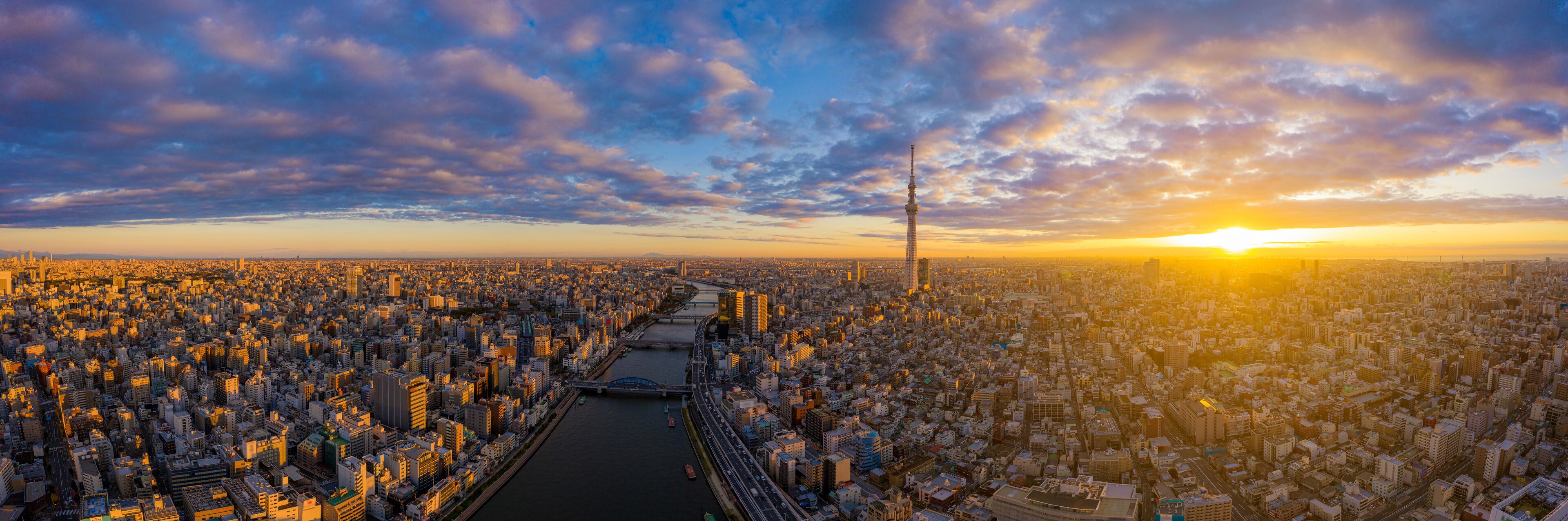 Une vue d’une ville au coucher du soleil, avec une rivière qui la traverse et un pont reliant les deux rives.