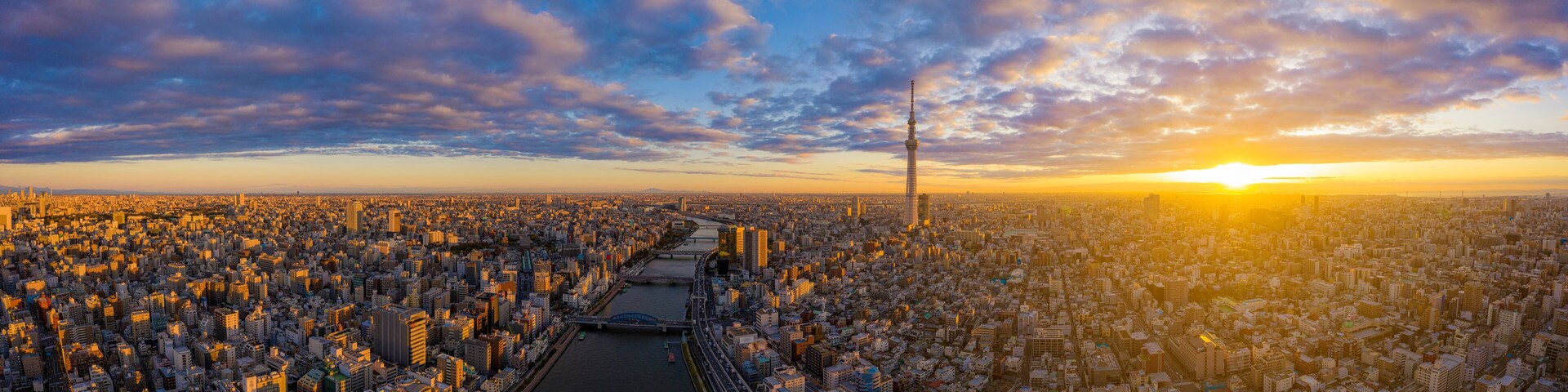 Paisagem urbana ao pôr do sol, com um rio serpenteando pela cidade e uma ponte ligando as margens.