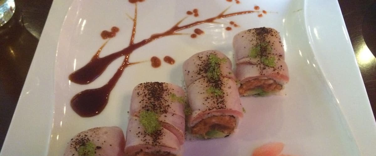 A white plate with rolled meat and vegetables, garnished with black pepper and green herbs.