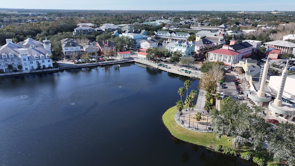 An aerial view of a waterfront area with a central lake, surrounded by colorful buildings and palm trees.