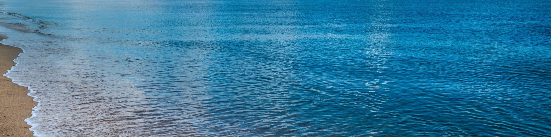 A calm sea with a sandy beach and a distant landmass under a partly cloudy sky.