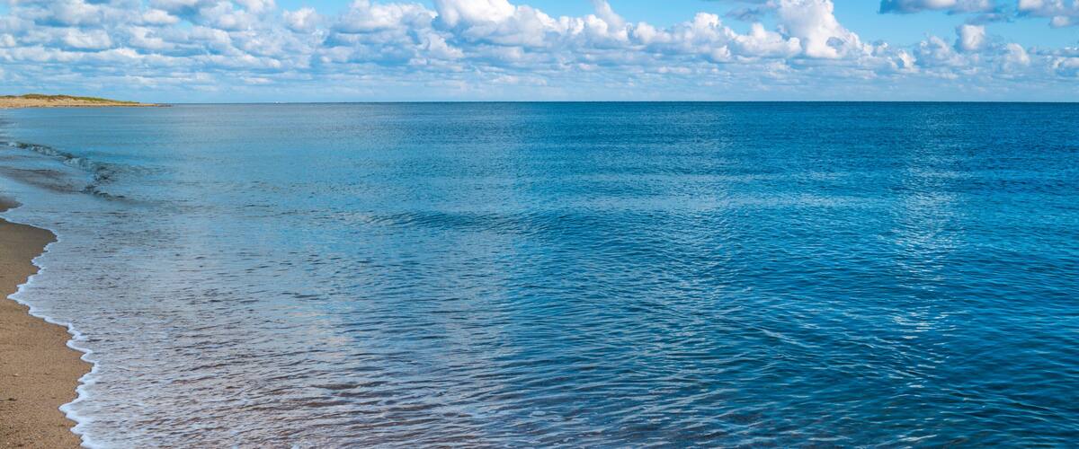 A calm sea with a sandy beach and a distant landmass under a partly cloudy sky.