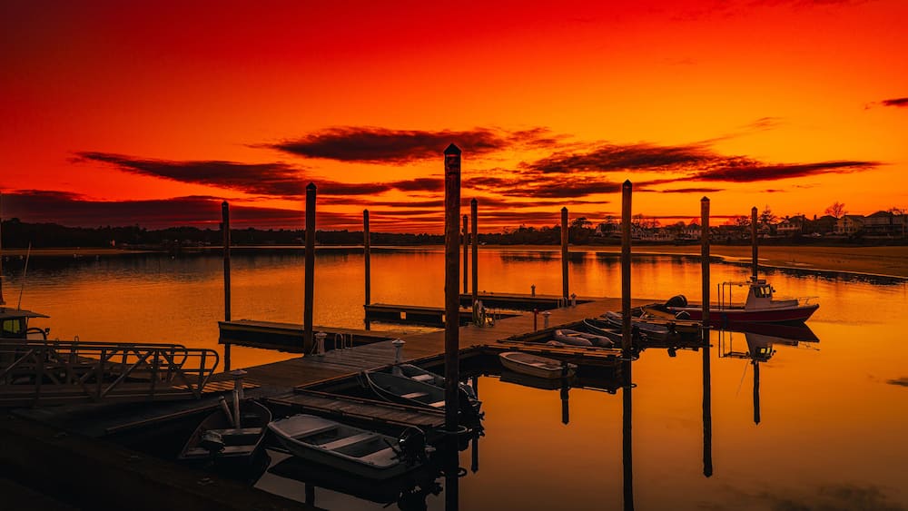A sunset over a calm harbor with boats docked at wooden piers.