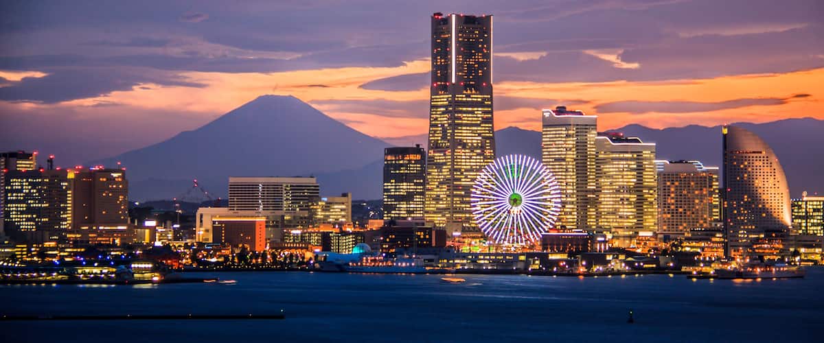 A city skyline with illuminated buildings and a large Ferris wheel against a sunset sky.