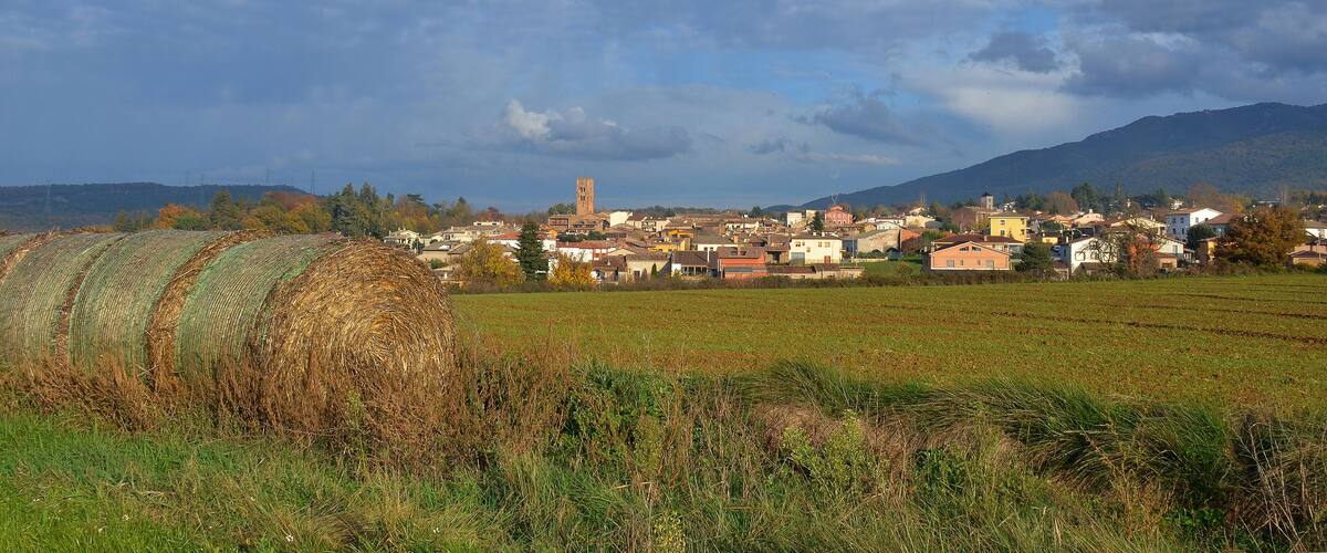 A rural landscape with a town, fields, and mountains in the background.
