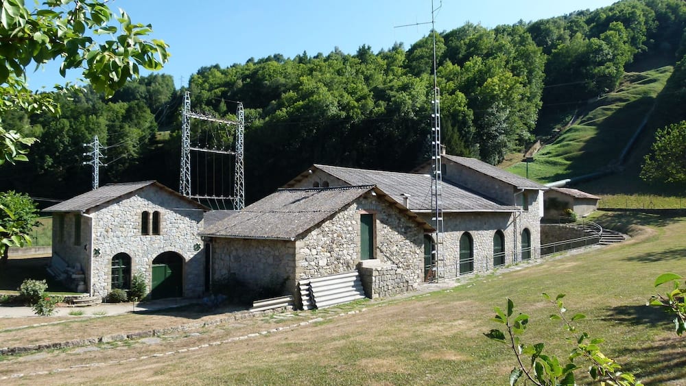 A stone building with a metal structure in a hilly area.