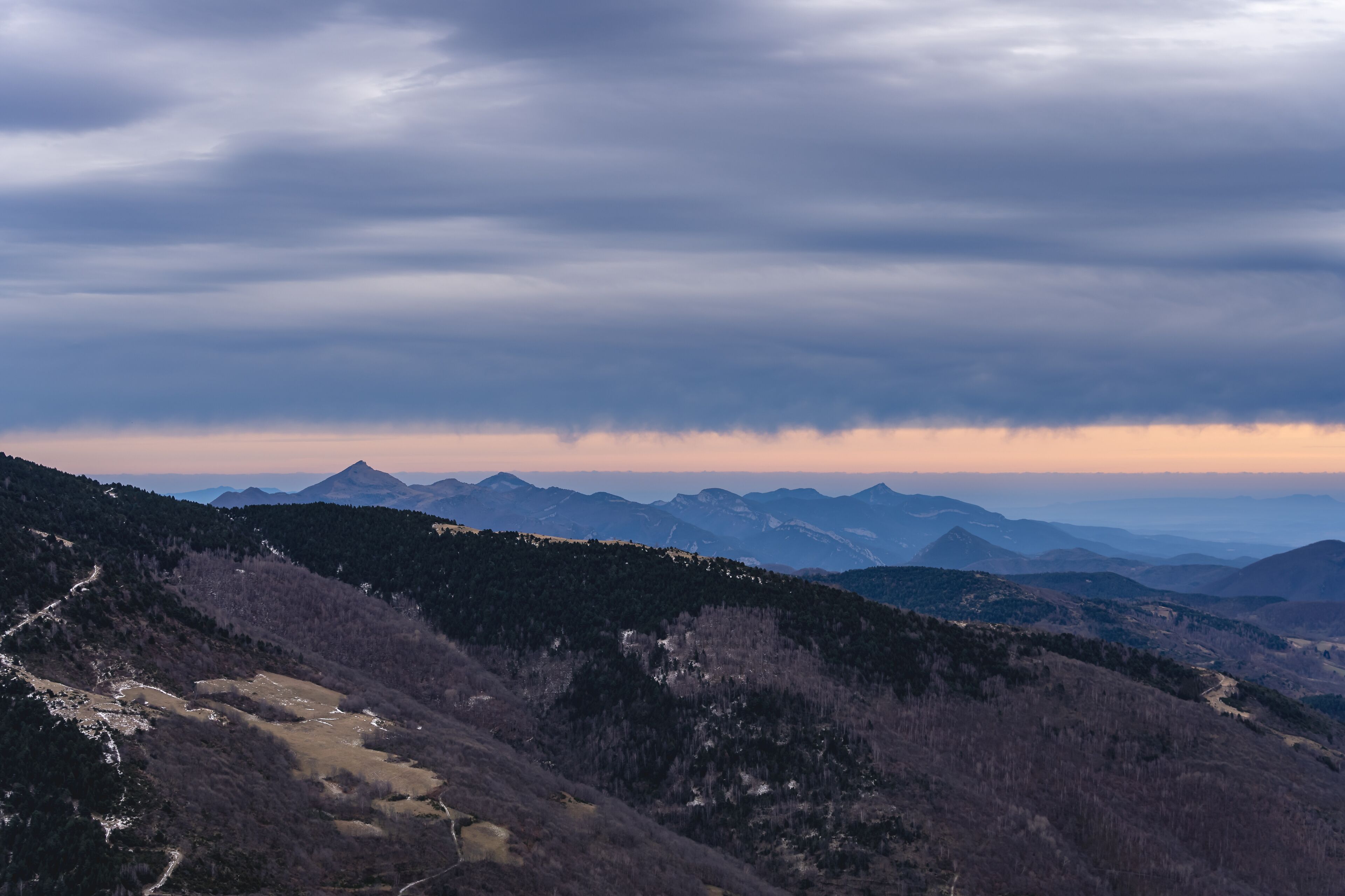 A mountainous landscape with a winding path and distant peaks under a cloudy sky.