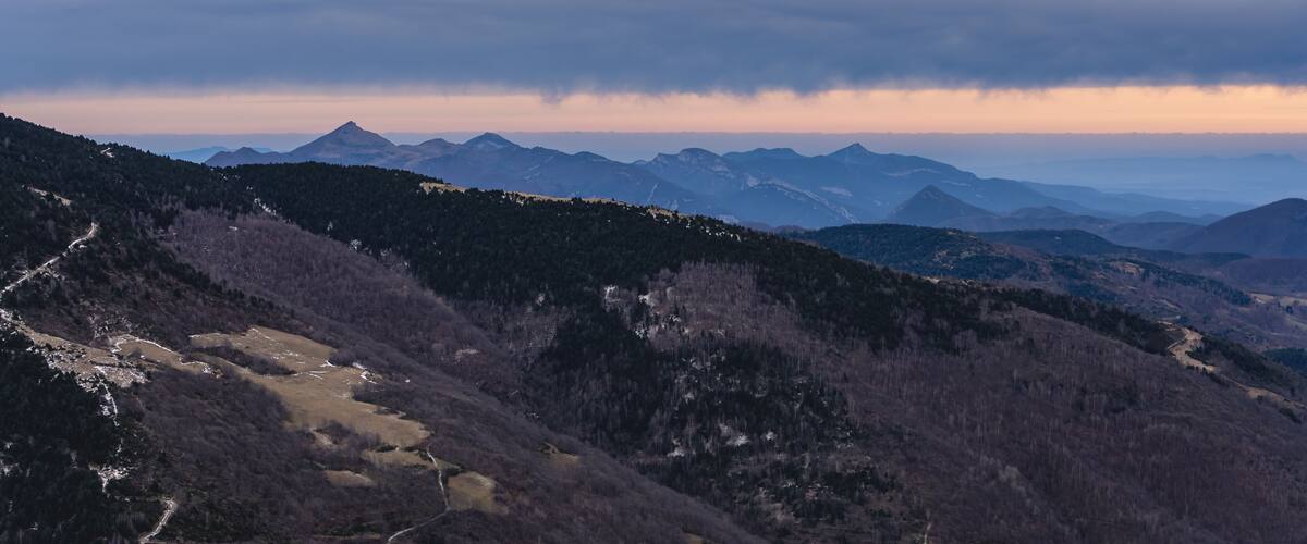 A mountainous landscape with a winding path and distant peaks under a cloudy sky.