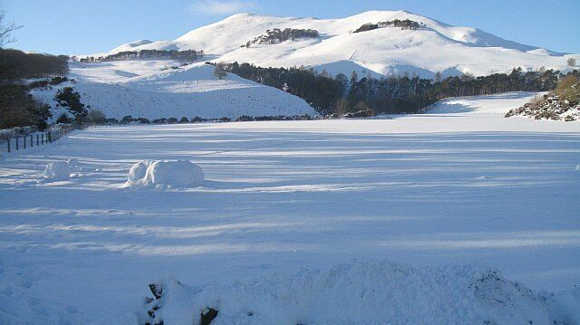 Un campo cubierto de nieve, con un muñeco de nieve y una montaña al fondo.