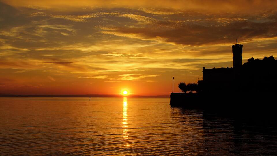 A sunset over a body of water with a silhouette of a tower and a building.
