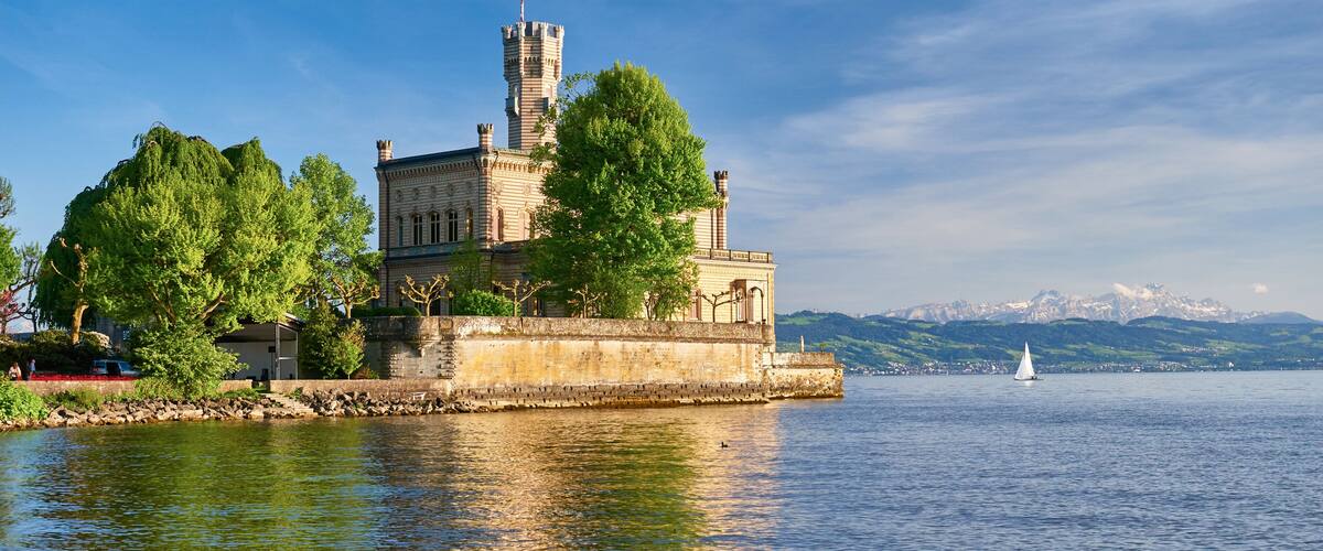 A historic castle on an island with a clear lake and mountains in the background.