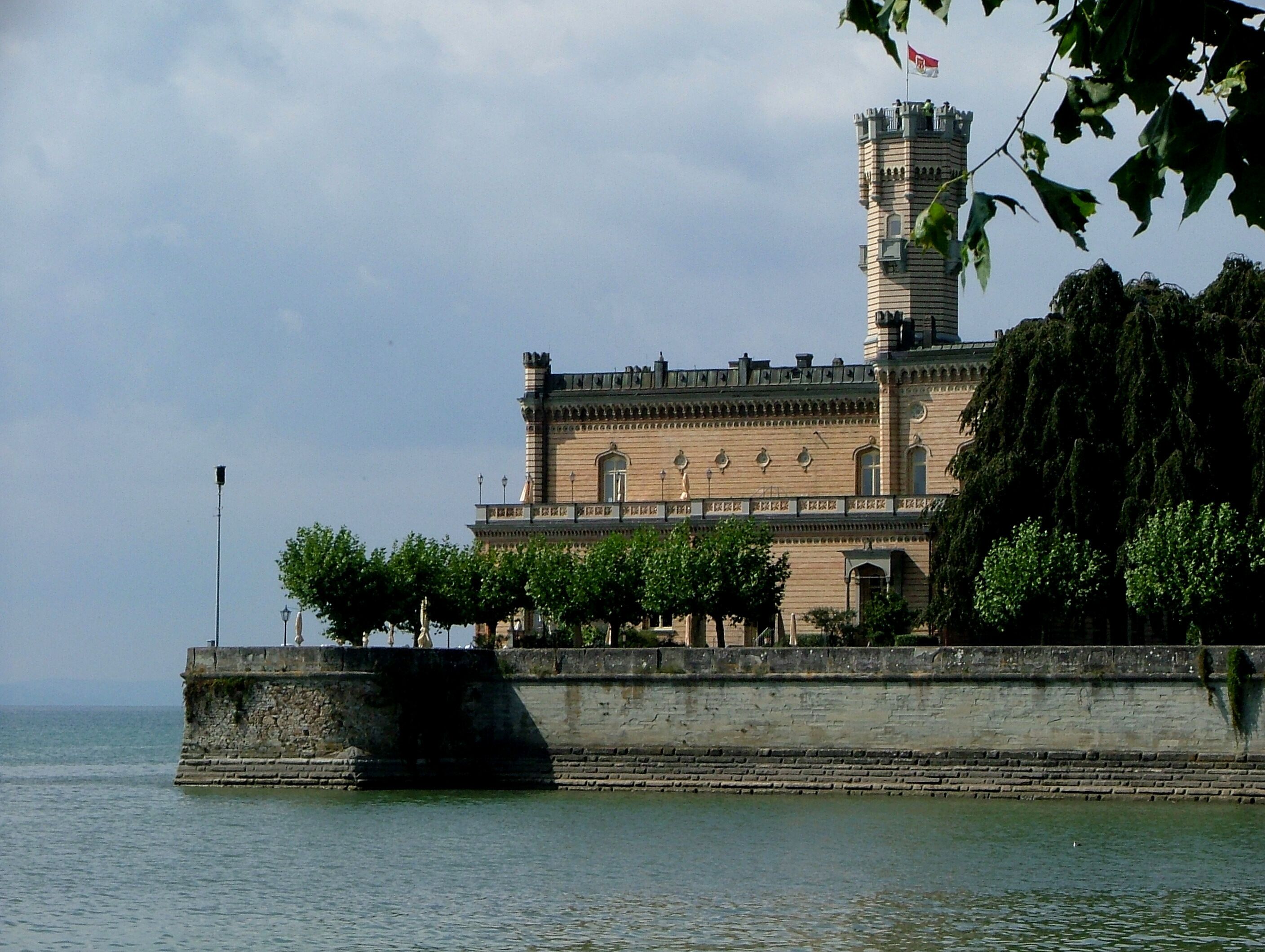 A historic building with a tower, a waterfront, and a stone wall.