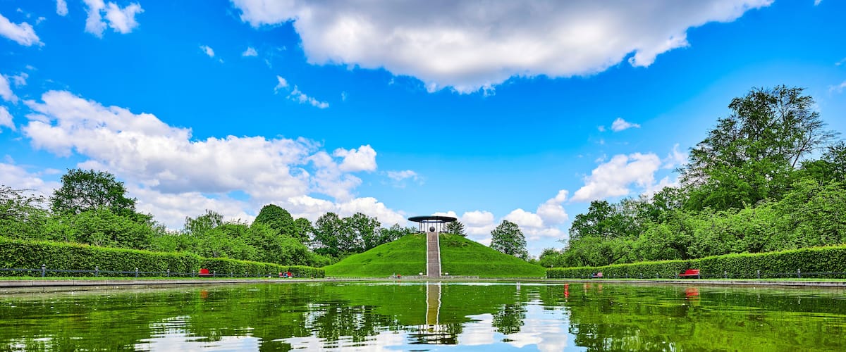 Public park in Berlin, Germany, in honor of the aviation pioneer Otto Lilienthal with a pool of water and reflections of the sky in the foreground and the monument on a hill in the background.
