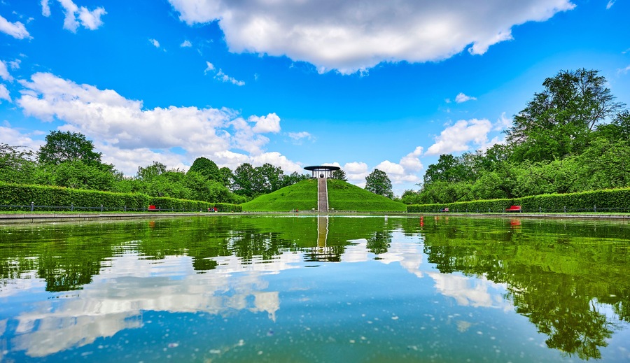 Public park in Berlin, Germany, in honor of the aviation pioneer Otto Lilienthal with a pool of water and reflections of the sky in the foreground and the monument on a hill in the background.