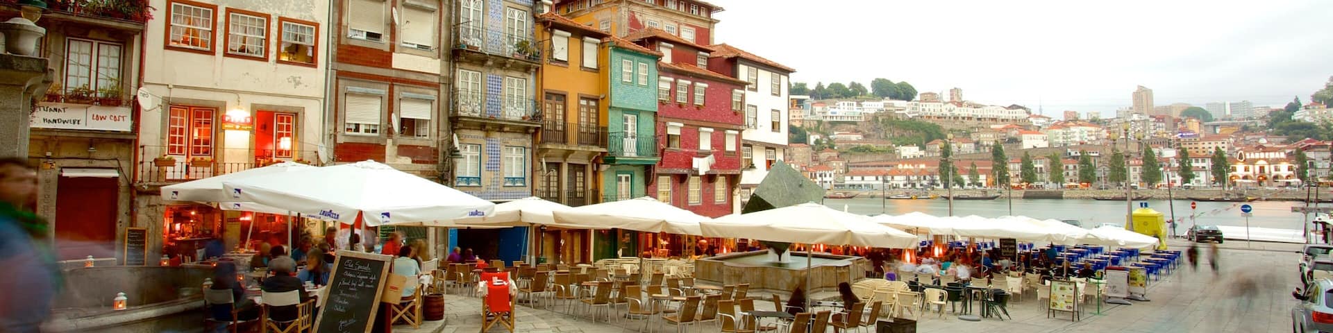 A bustling riverside square with colorful buildings, outdoor cafes, and a view of the cityscape in the background.