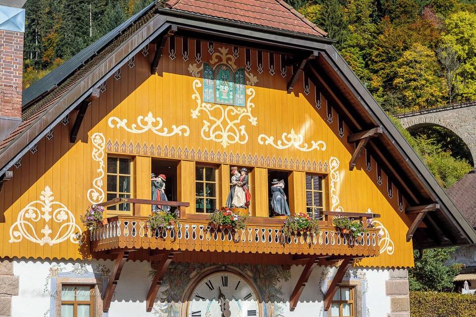 Una casa de fusta tradicional amb detalls tallats i un balcó amb cistells de flors.