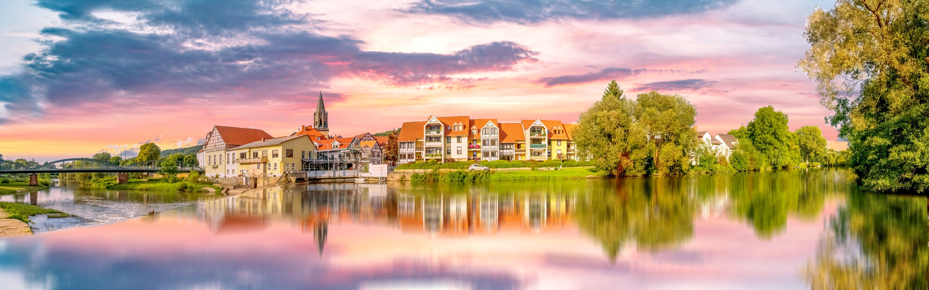 A riverside town with historic buildings, a church, and a bridge.