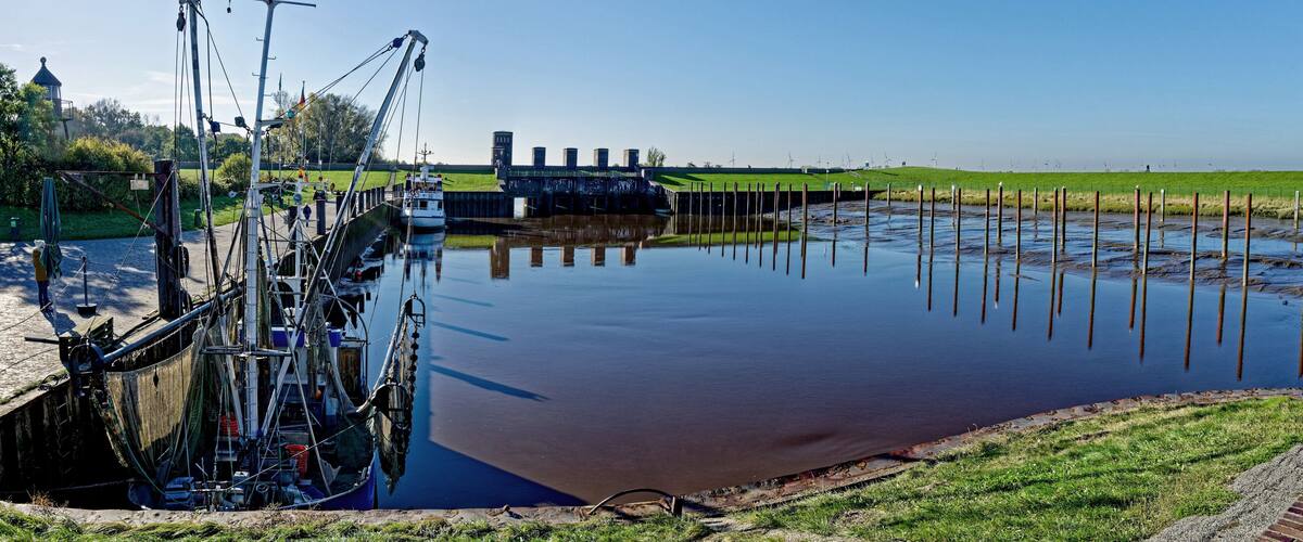 A calm river with a lock system, green grass, and wind turbines in the background.
