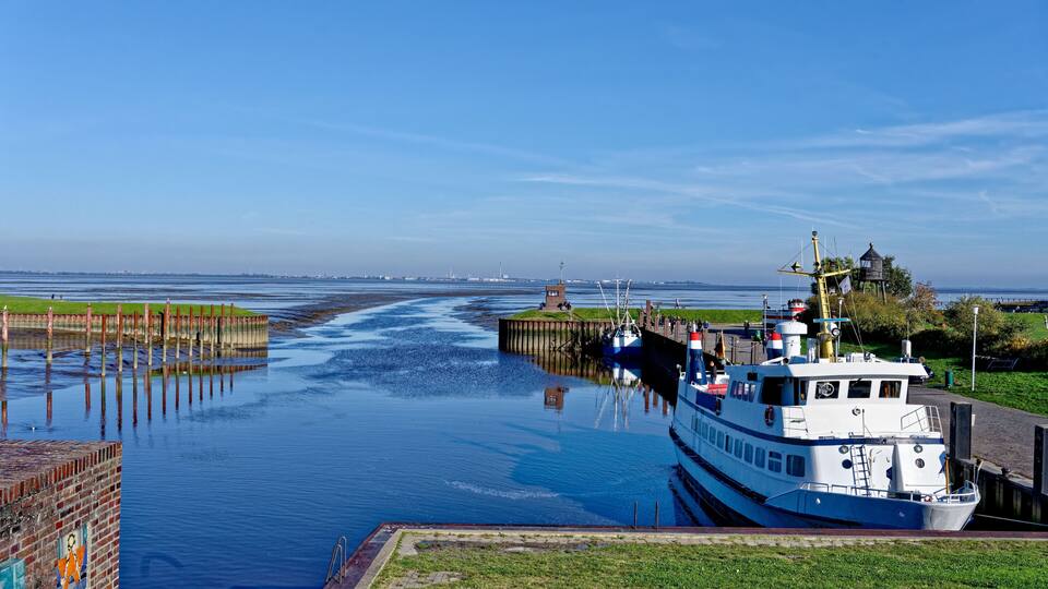 A river with a boat docked at a pier, a lighthouse in the distance, and a small island with a structure.