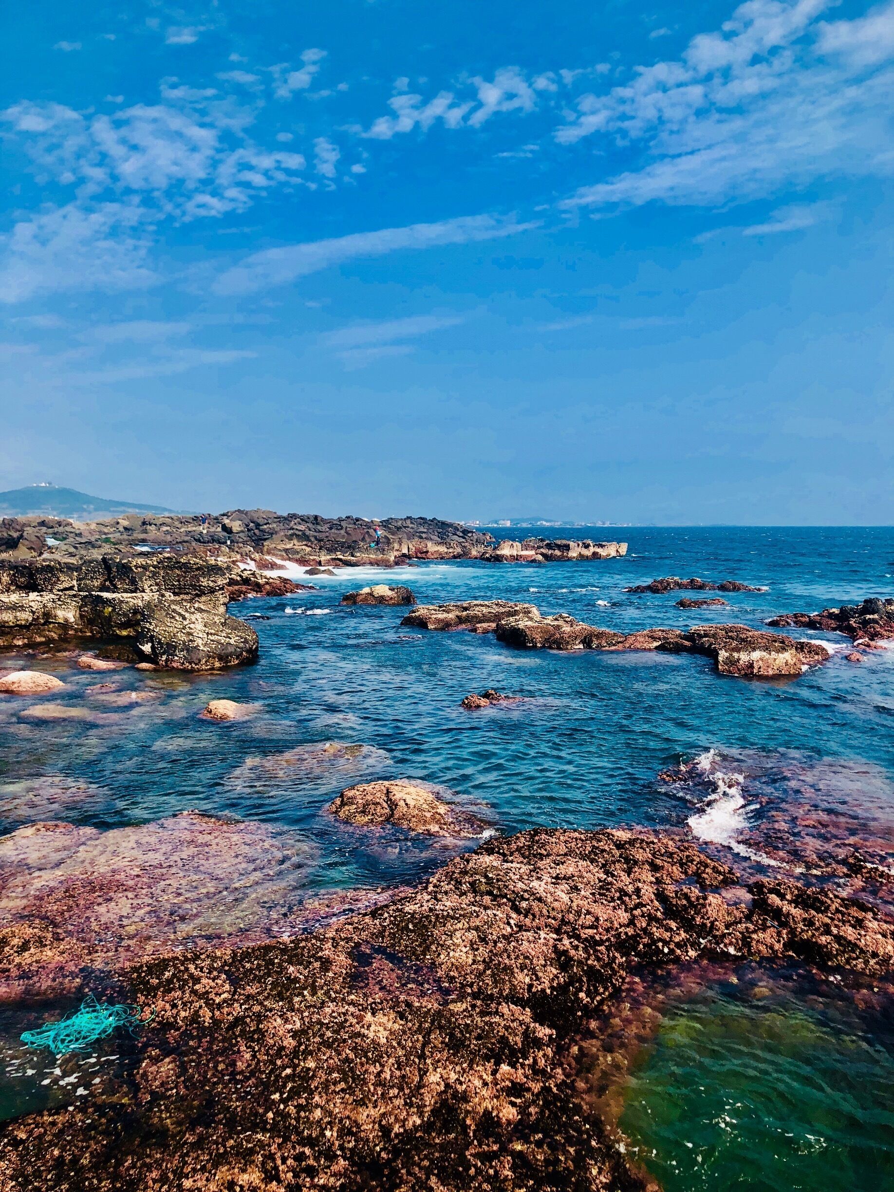 A rocky coastline with clear blue waters and scattered rocks.