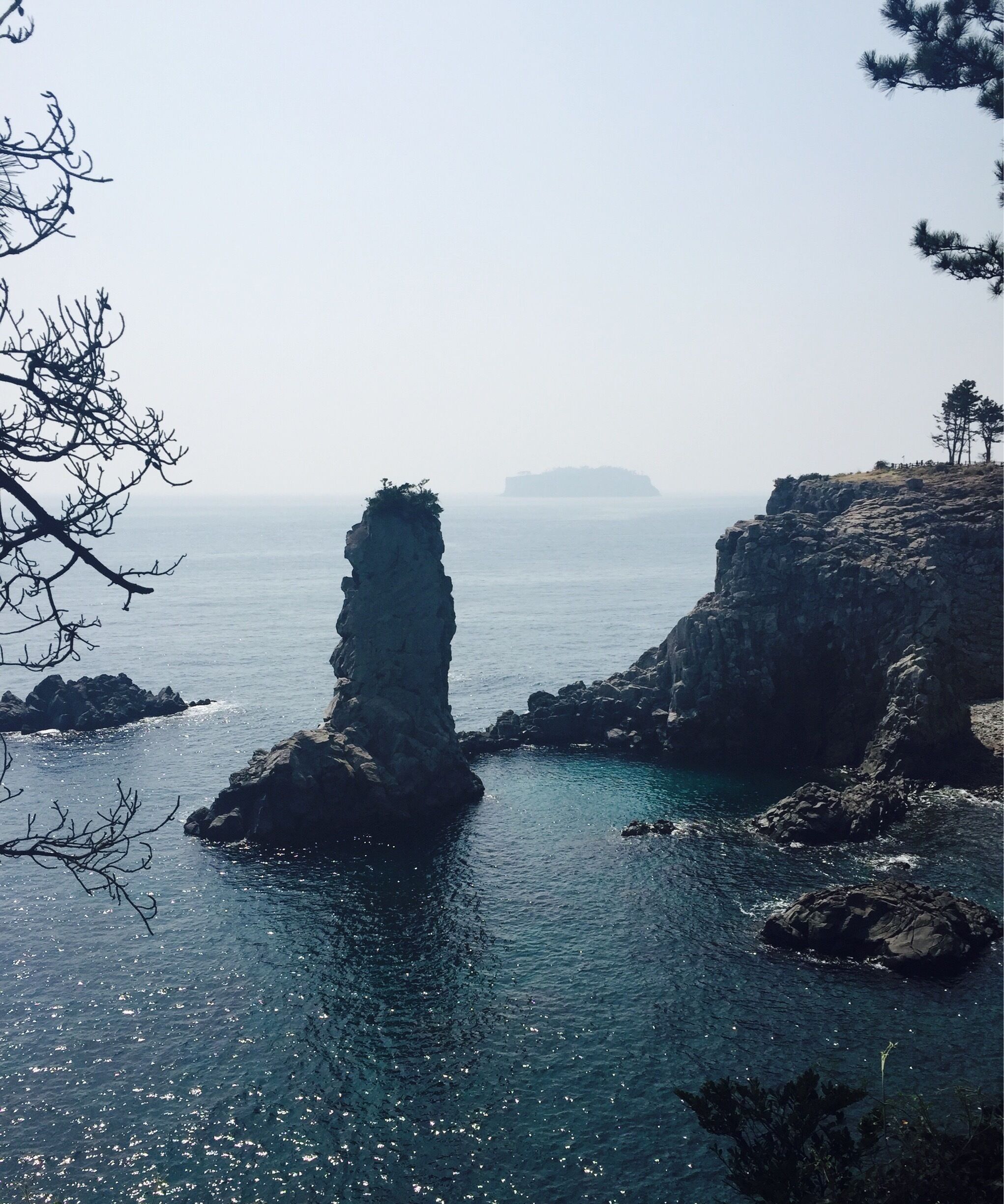 A coastal landscape with a prominent rock formation in the sea, surrounded by smaller rocks and clear water.