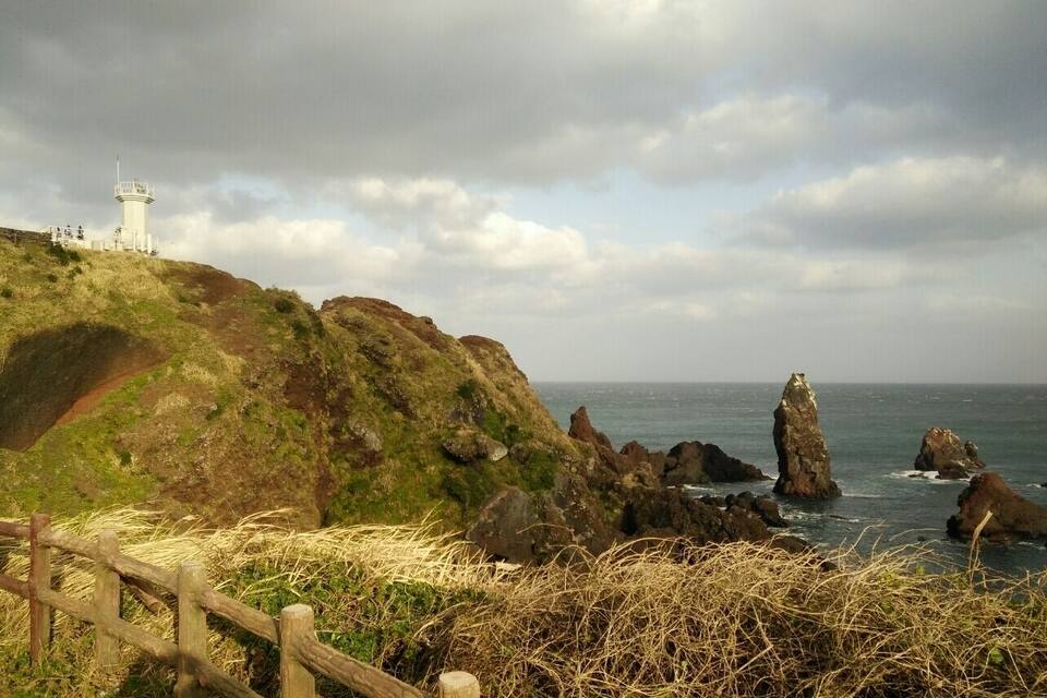 A coastal landscape with a lighthouse, rocky outcrops, and a wooden fence.