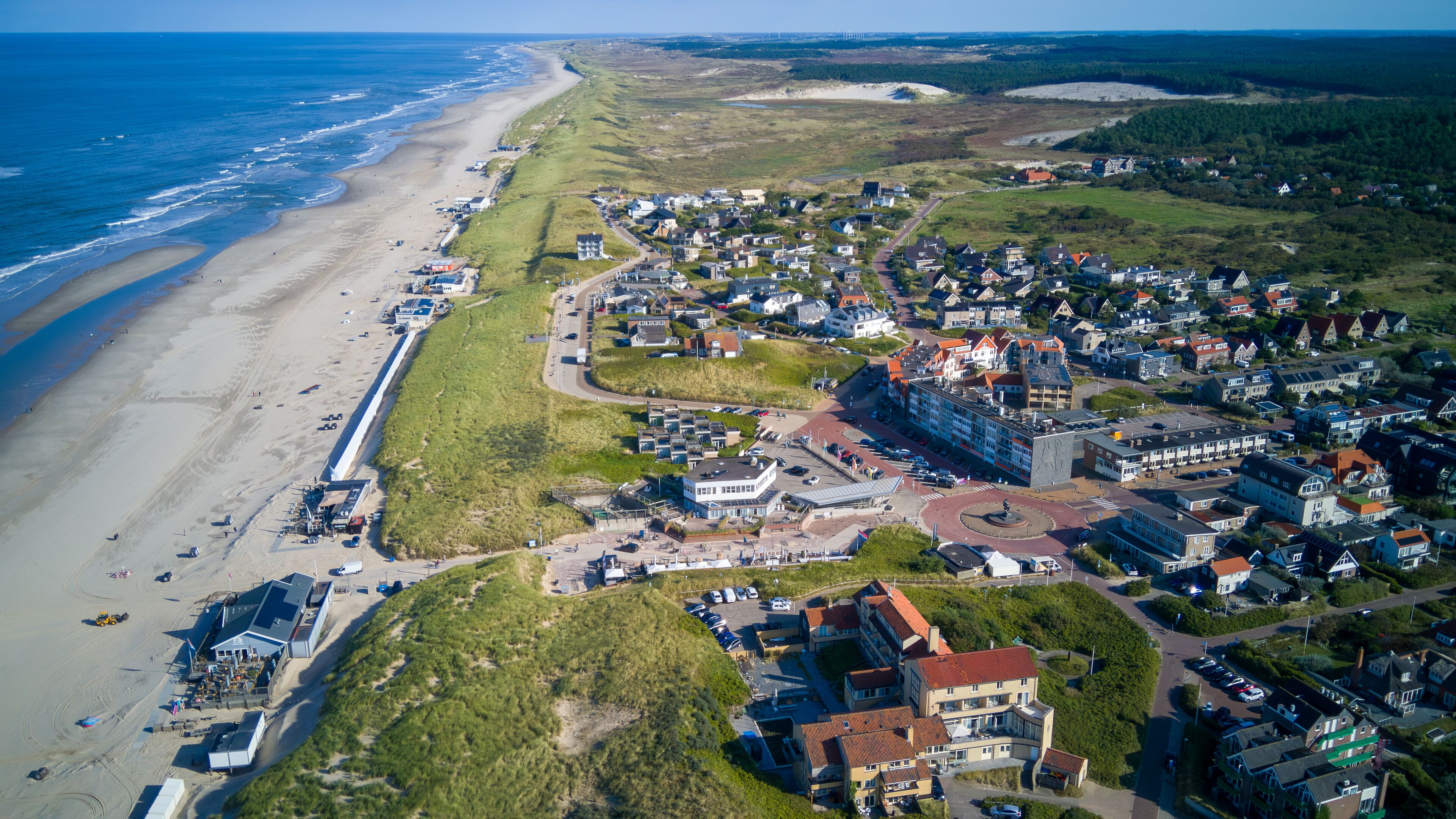 A coastal town with a beach, houses, and a large building complex.