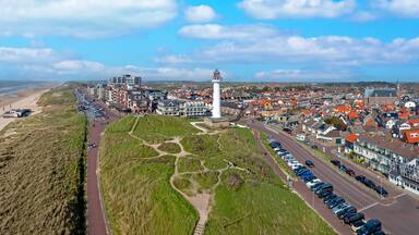 Een kustplaats met een strand, een vuurtoren en een weg omzoomd met huizen.