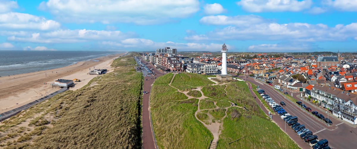 A coastal town with a beach, a lighthouse, and a road lined with houses.