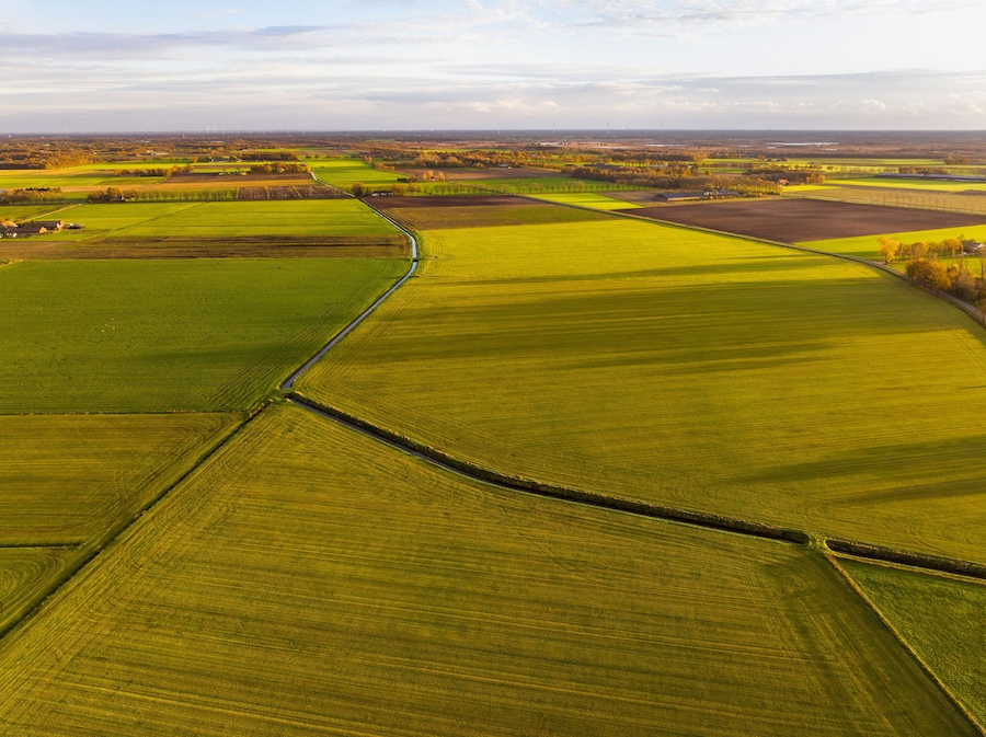 Aerial view of warm evening light over beautiful meadows and canalized stream in serene countryside, Asten, Netherlands.