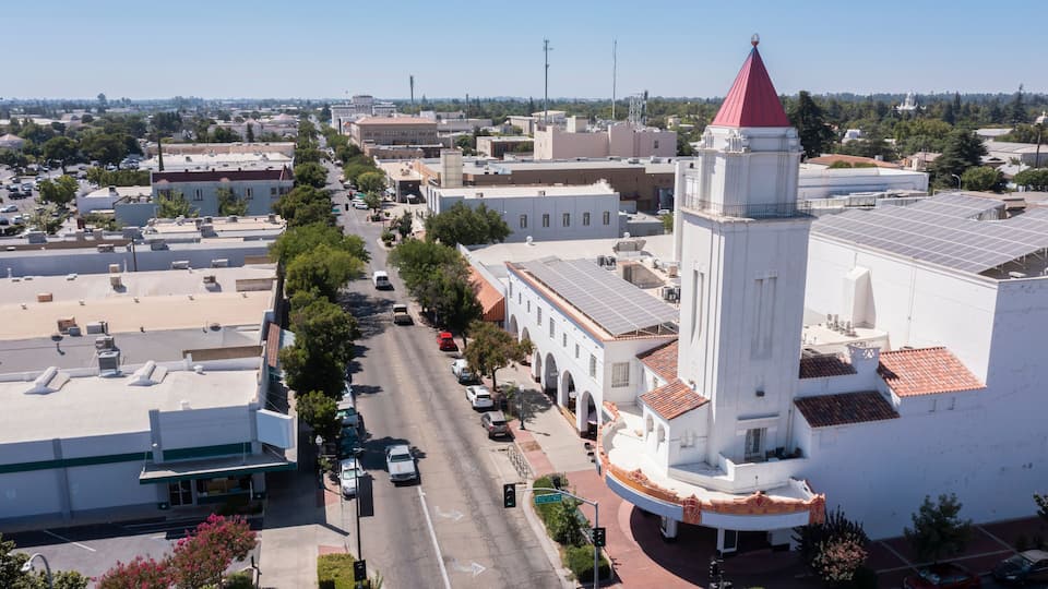 A street lined with buildings, a prominent white tower with a red roof, and solar panels on rooftops.