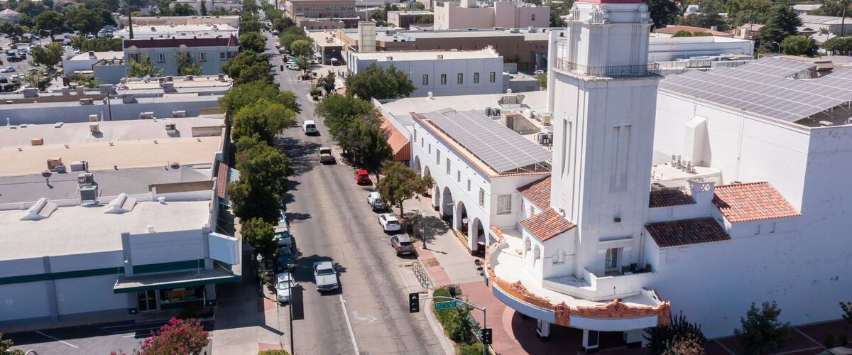 A street lined with buildings, a prominent white tower with a red roof, and solar panels on rooftops.