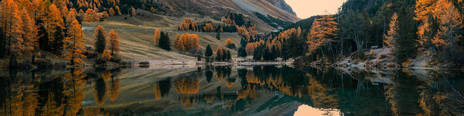 autumn colours and sunrise with reflections in calm mountain lake in the Swiss Alps