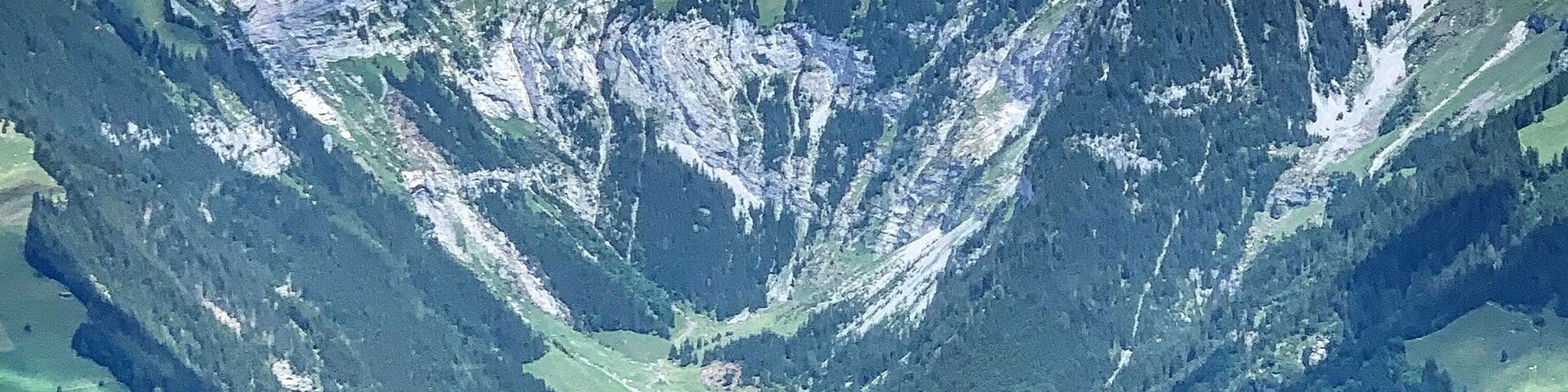 Un paisaje montañoso con un valle, campos verdes y un pueblo pequeño.
