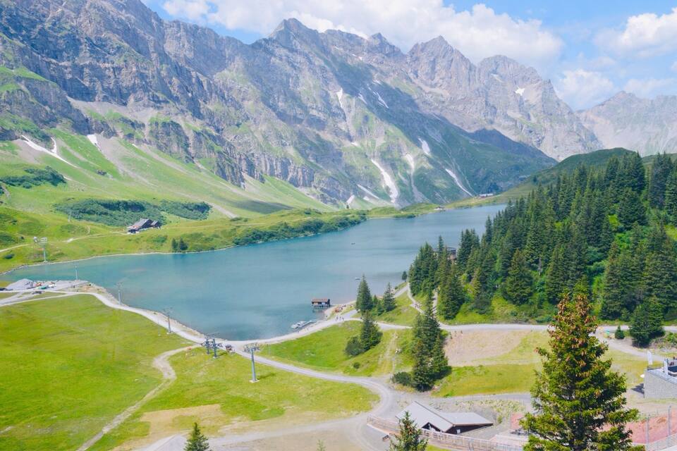 Un paysage montagneux avec un lac, des champs verdoyants et un petit bâtiment situé près du bord de l’eau.