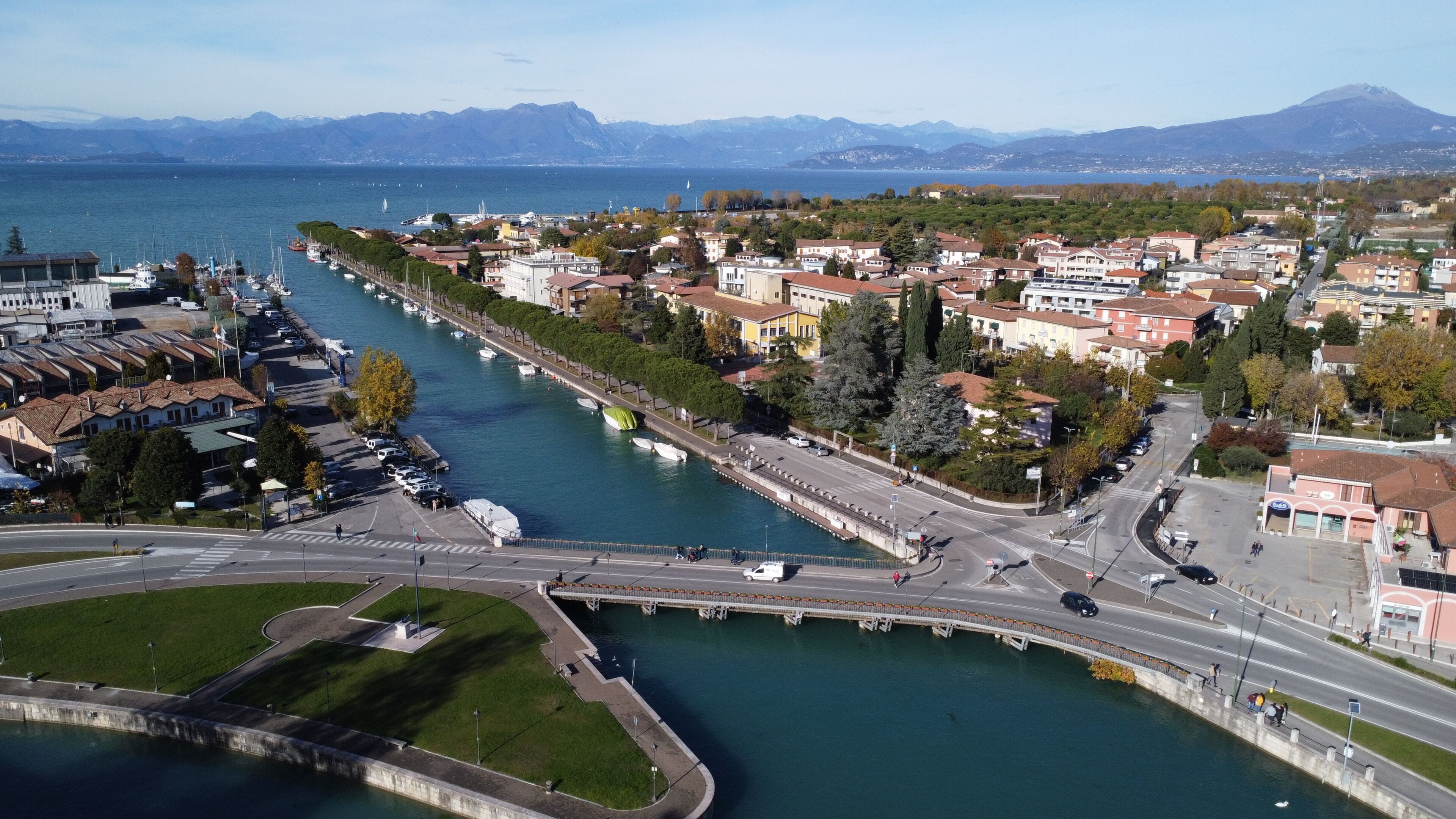 Uma cidade costeira com um porto de recreio, uma ponte e montanhas ao fundo.