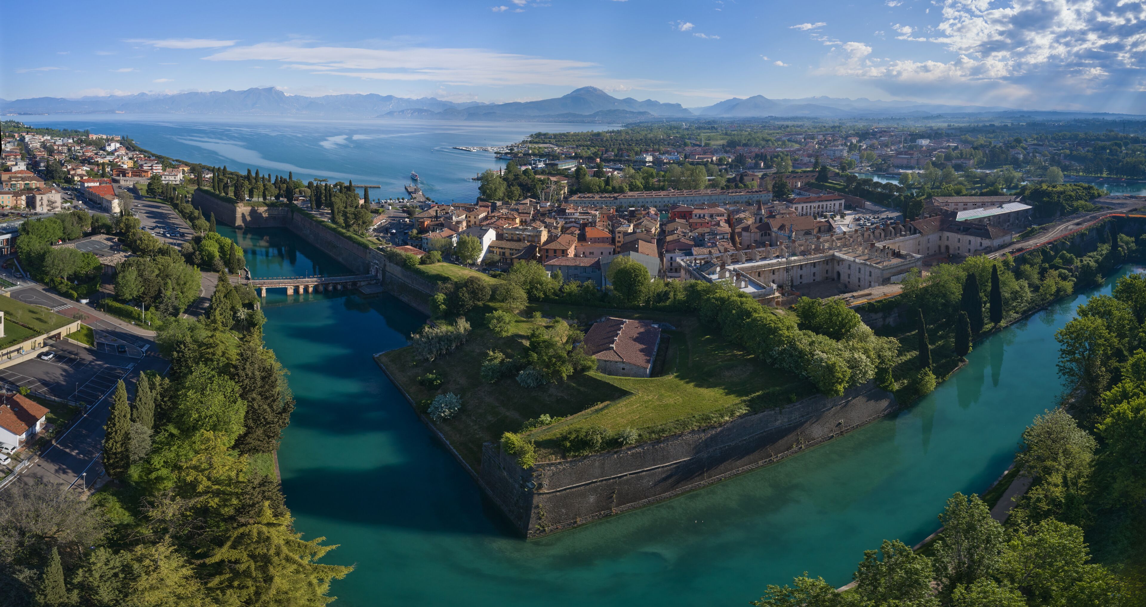 A coastal city with a fortified island, a river, and a mountainous backdrop.