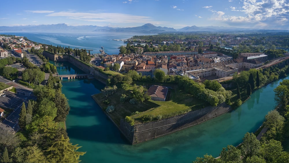 A coastal city with a fortified island, a river, and a mountainous backdrop.