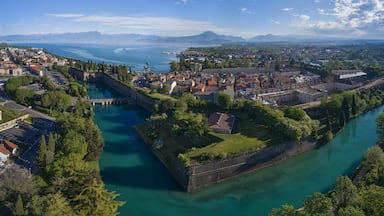 Uma cidade costeira com uma ilha fortificada, um rio e um cenário montanhoso.