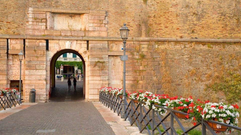 An arched stone gateway with a metal fence and flower planters on either side.