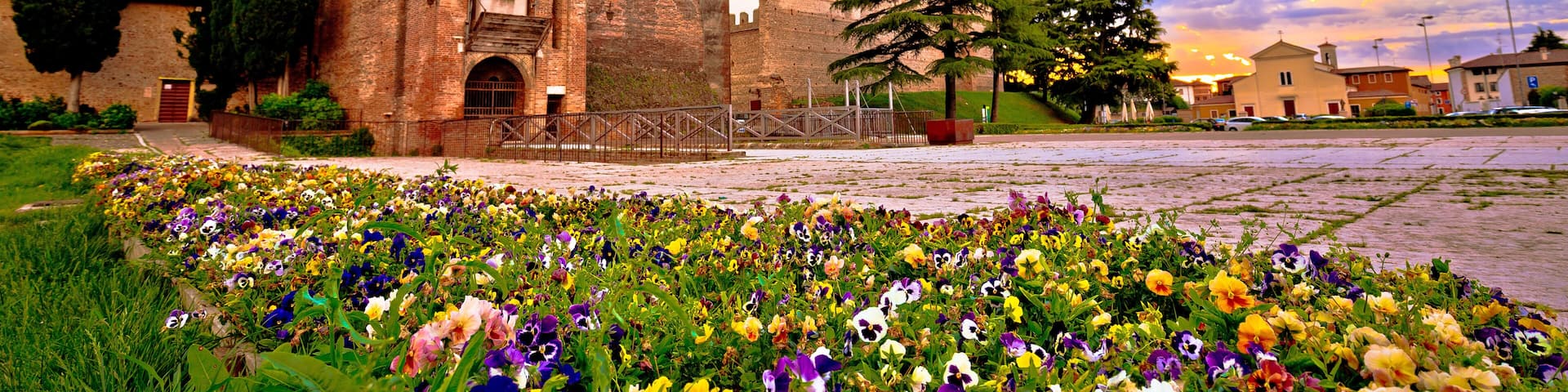 A historic castle with a clock tower, surrounded by a vibrant flower garden and a clear sky.
