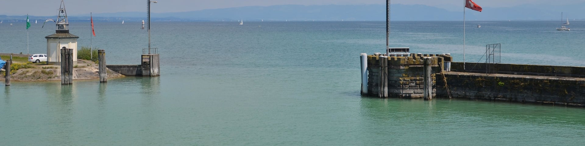 A coastal scene with a lighthouse, a pier, and sailboats on the water.