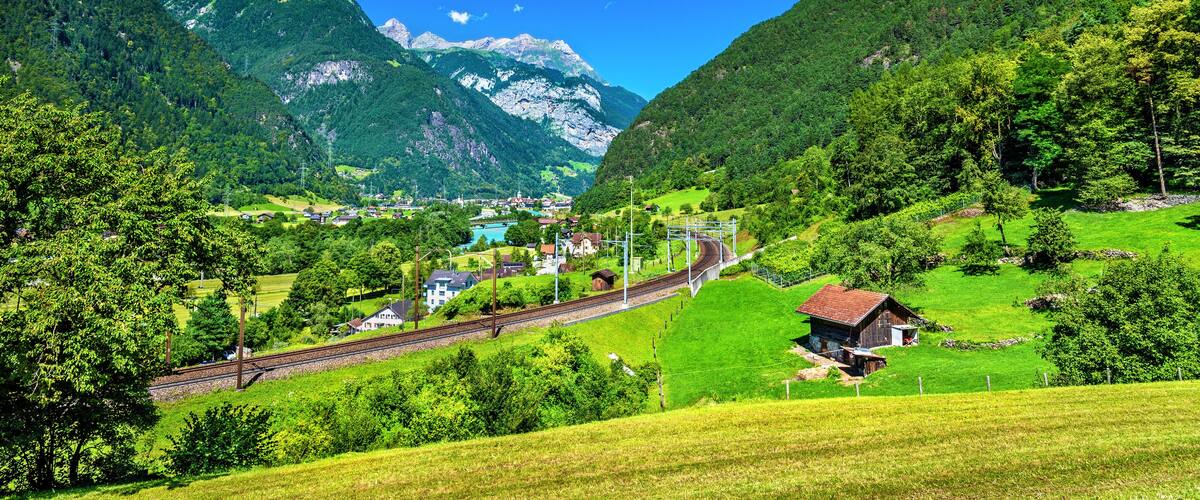 A mountainous landscape with a railway track, green fields, and a small village.