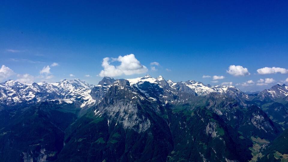 A mountainous landscape with snow-capped peaks, a valley with greenery, and a lake.