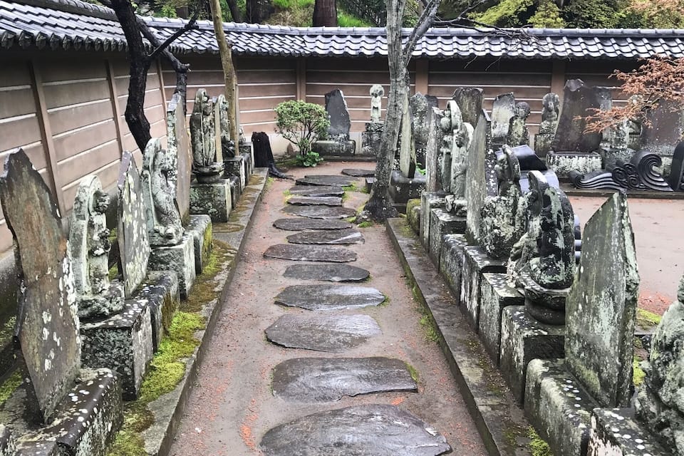 Ein traditioneller japanischer Friedhof mit steinernen Laternen und einem Gebäude mit Schindeldach.