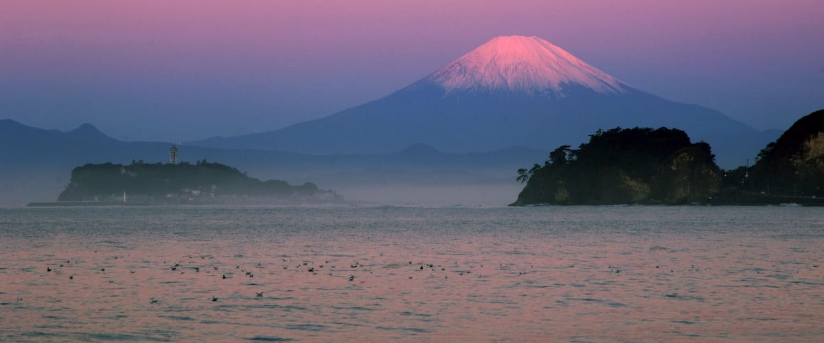 A sunset over a body of water with a mountain in the background.