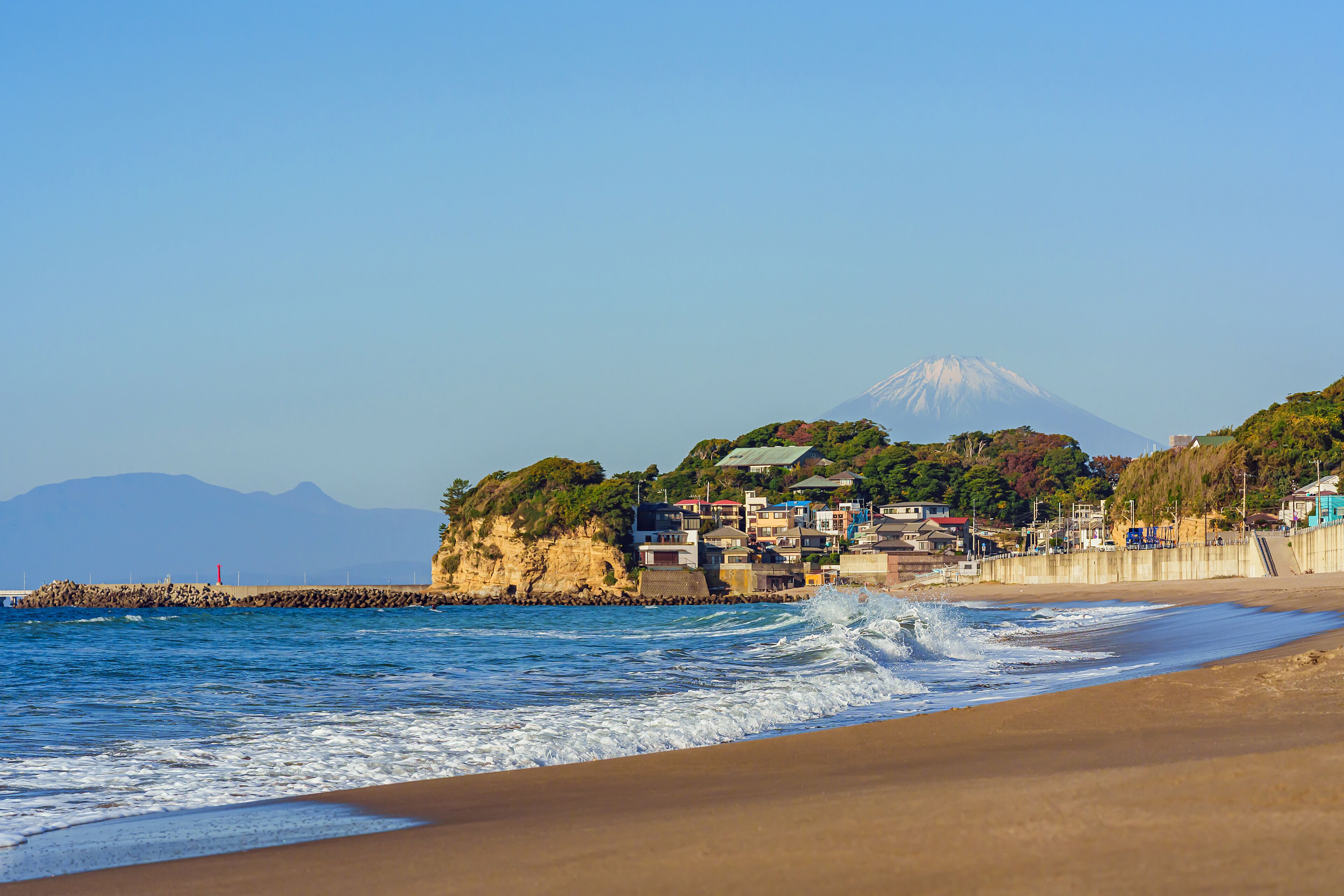 Una playa con olas, un pueblo costero y una montaña al fondo.
