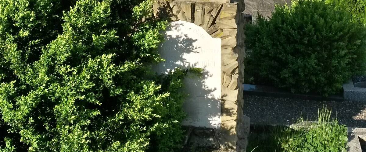 A stone angel statue with inscriptions, surrounded by lush greenery and residential buildings.