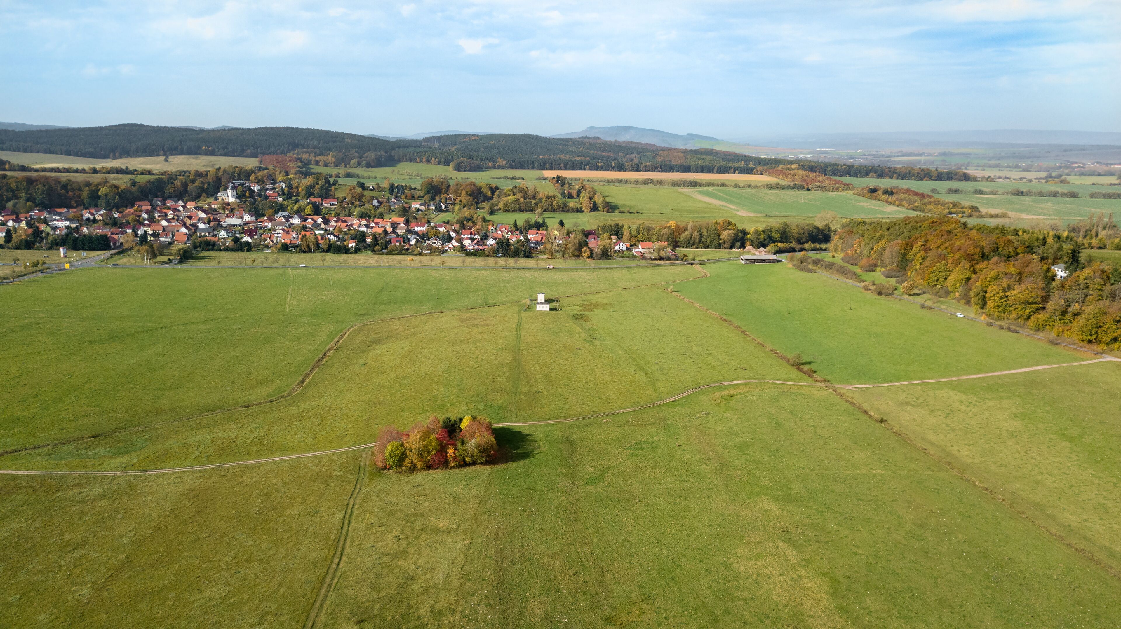An aerial view of a rural area with a small village, green fields, and distant hills.